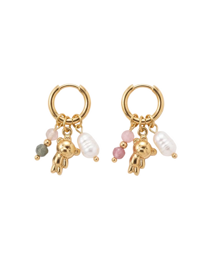 A pair of gold hoop earrings with dangling charms, including small gold teddy bear charms, white pearl beads, pink beads, and a single green bead, displayed on a clean white background.